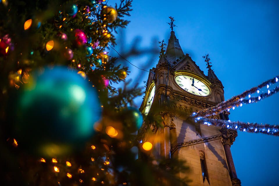 The clock tower in Leicester decorated for Christmas behind a Christmas tree covered in tinsel and baubles