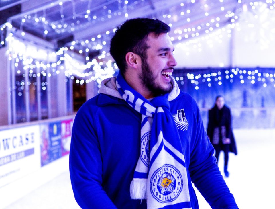 A man smiling wearing a Leicester City Football Club scarf while ice skating