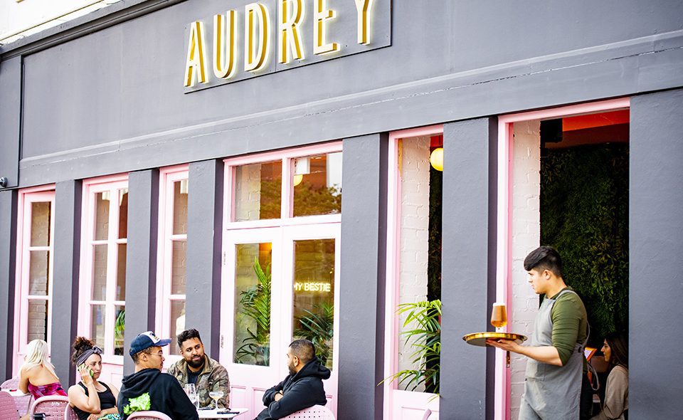 Groups of people sat outside of Audrey in Leicester as a server carries a drink on a tray